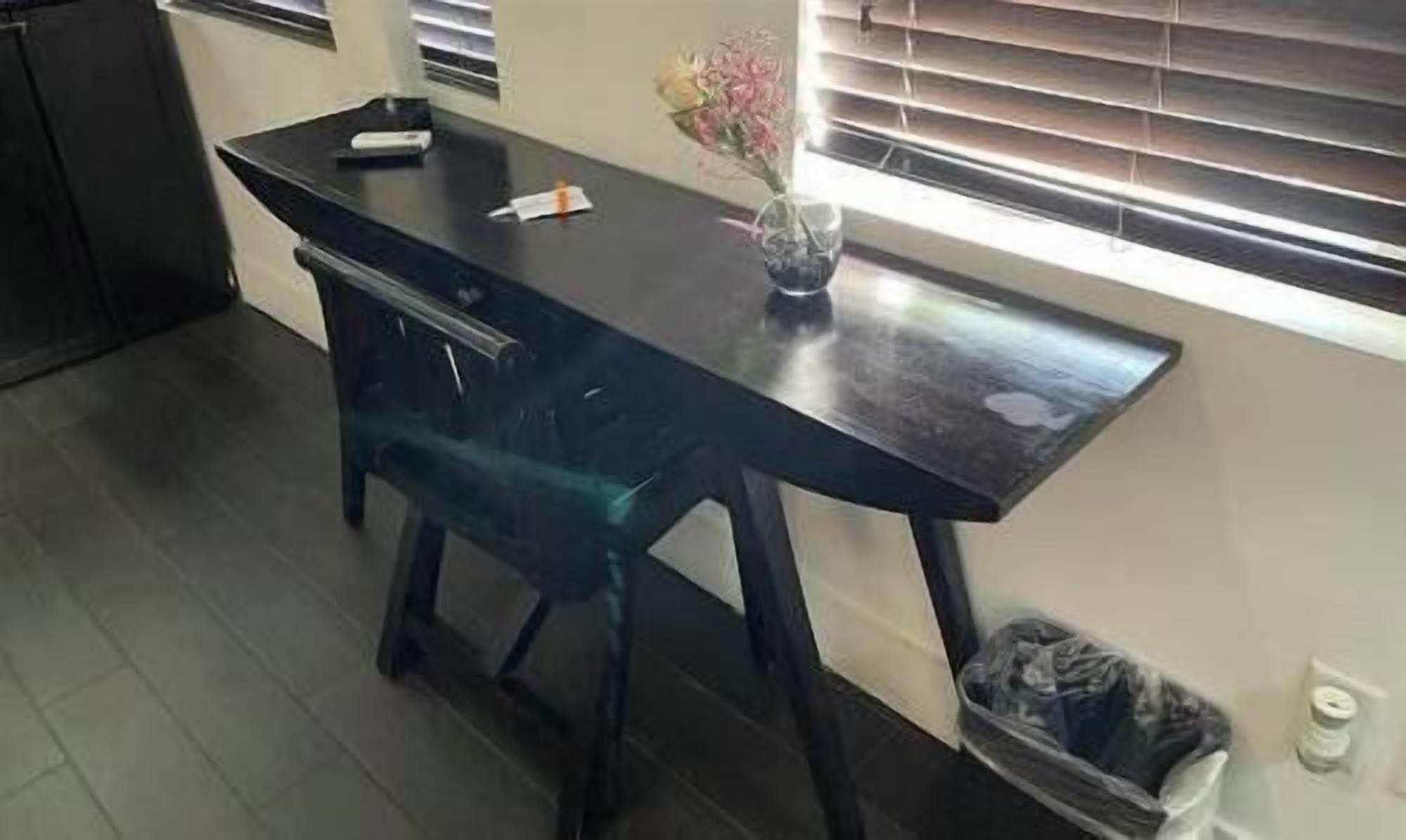 Une cuisine avec un plan de travail foncé, un vase rempli de fleurs et une poubelle.
