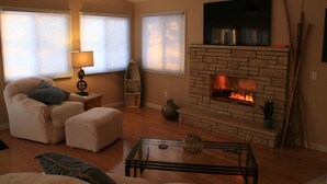 Una sala de estar con chimenea, un sofá, una mesa de centro y un televisor montado en la pared.
