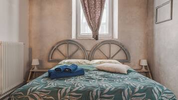 Un dormitorio con cama, dos lámparas de noche, un radiador y una ventana con cortinas.