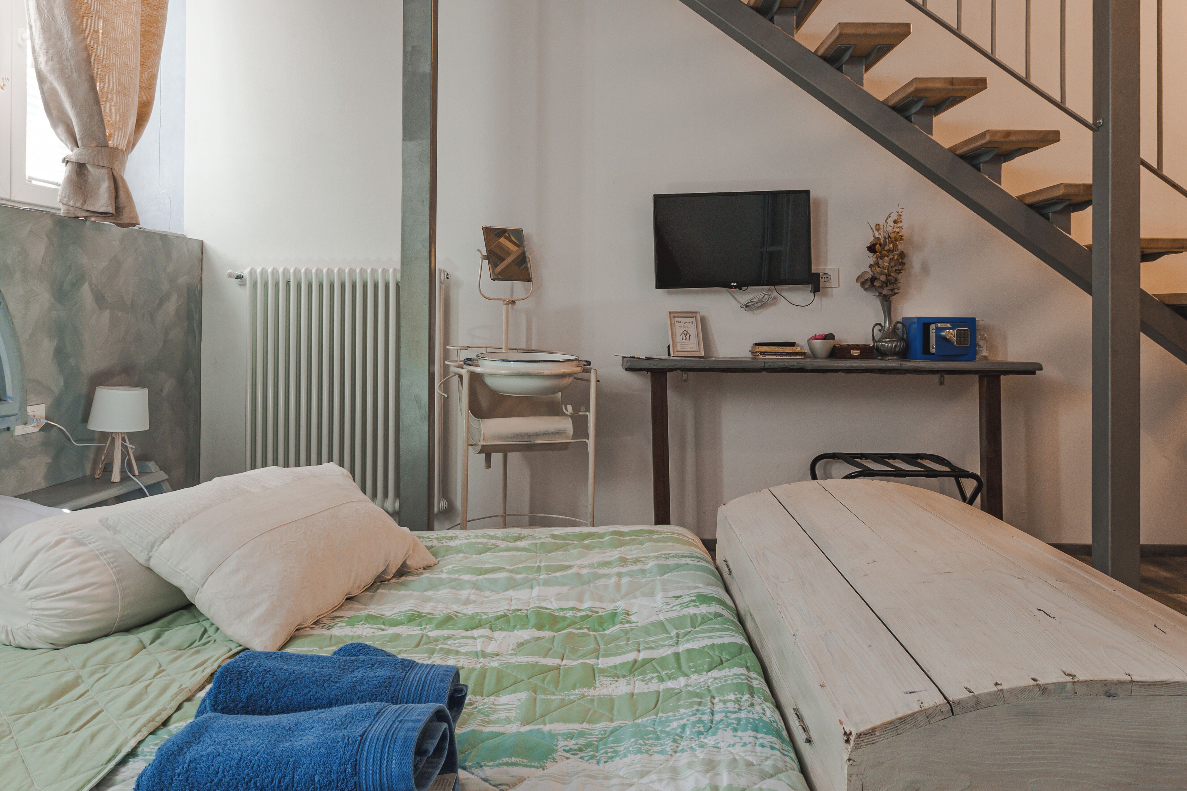 A bedroom with a bed, a desk, a chair, a radiator, a television, and a staircase.