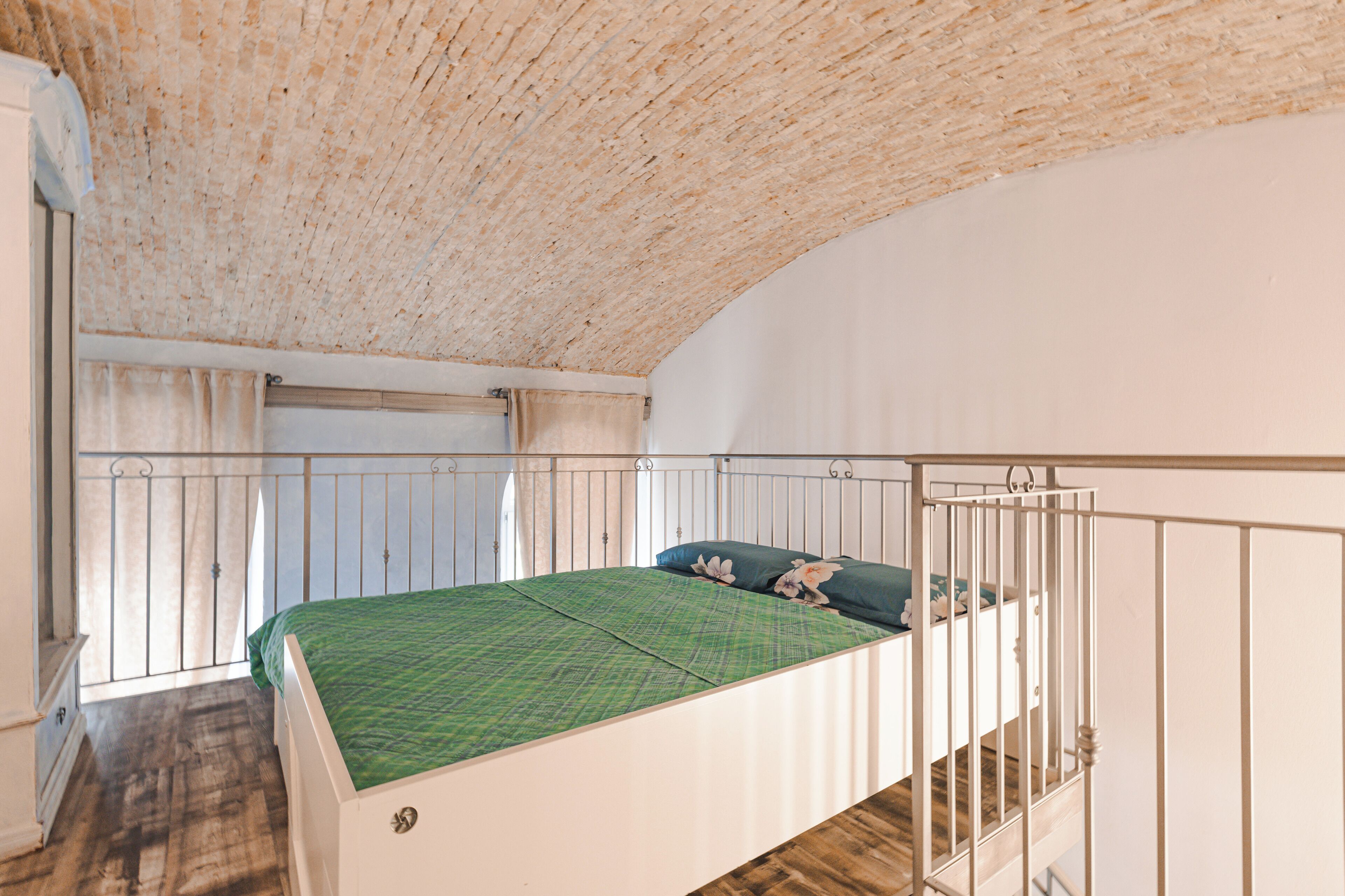 Une chambre avec un plafond en bois, un lit recouvert d’une couverture verte et une fenêtre avec des rideaux.