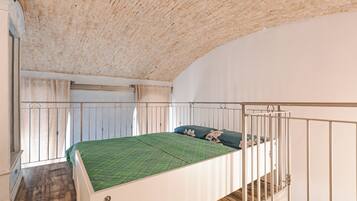 Une chambre avec un plafond en bois, un lit recouvert d’une couverture verte et une fenêtre avec des rideaux.