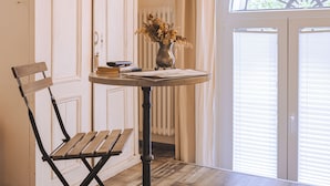A room with a wooden bench, a small table with a vase of dried flowers, and a window with blinds. - Trieste Art Loft (Trieste)