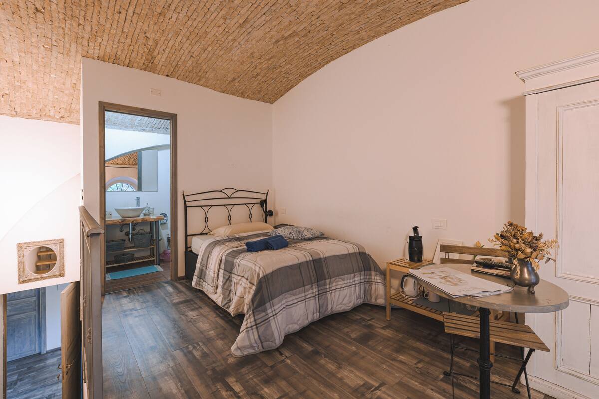 A bedroom with a bed, bedside table, and a small table with a vase.