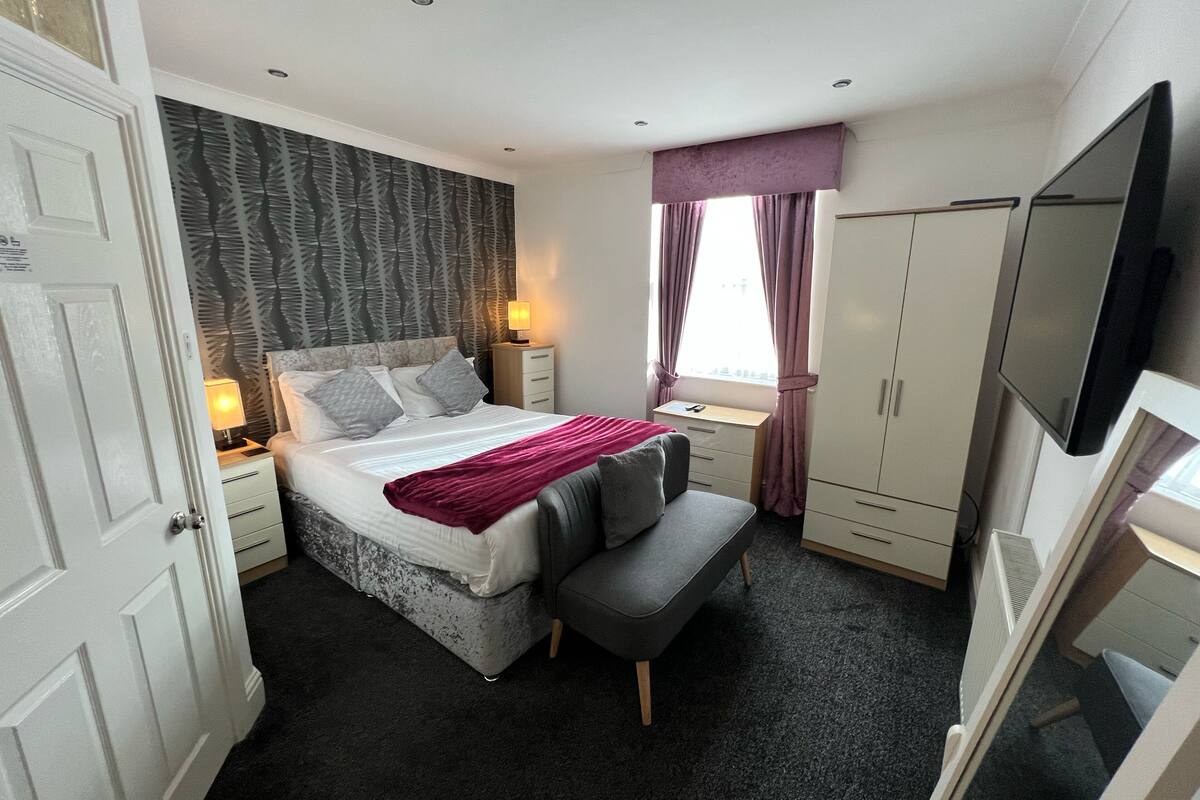 A bedroom with a bed, bedside table, desk, chair, wardrobe, and a TV.
