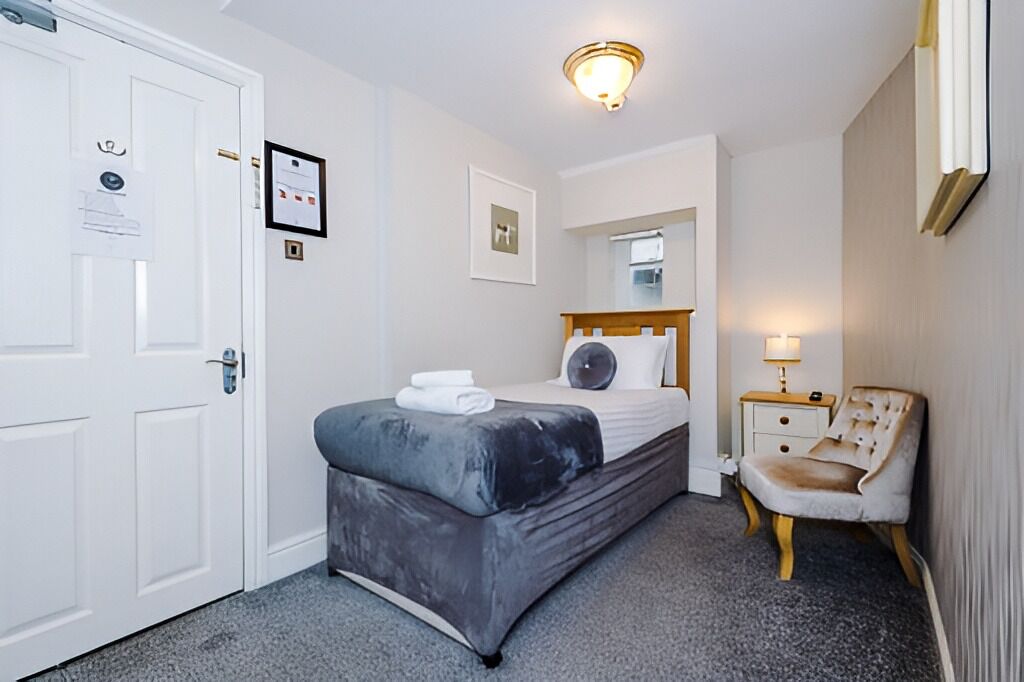 A hotel room with a bed, a chair, a nightstand, a mirror, and a door.