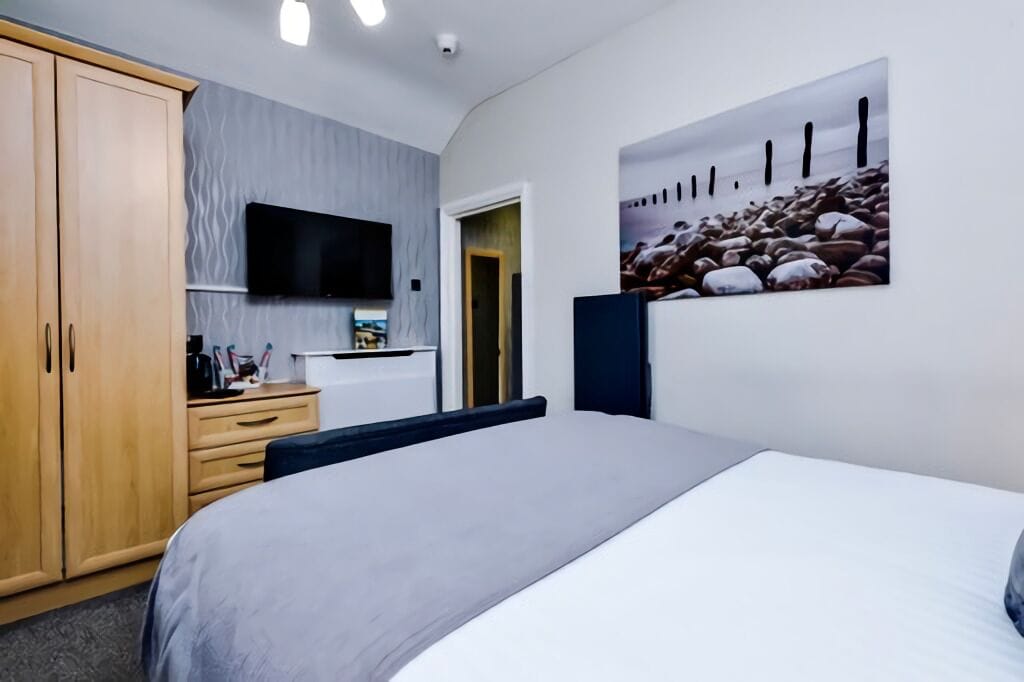 A hotel room with a bed, a wardrobe, a desk with a flat-screen TV, and a painting on the wall.