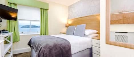 Un dormitorio con cama, televisión, ventana con cortinas, cabecera y pared con diseño geométrico.