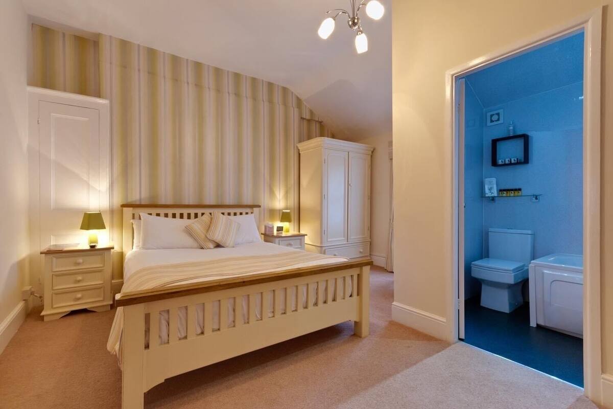 A bedroom with a bed, bedside tables, a wardrobe, and a bathroom visible through an open door.