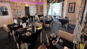 A restaurant with black and white patterned wallpaper, multiple tables with set dining ware, and a chandelier. - Lawton & Lauriston Court (Llandudno)