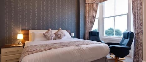 A hotel room with a large bed, a bedside table with a lamp, a chair, and a window with curtains.