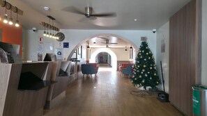 Um lobby de hotel com balcão de recepção, área de estar, árvore de Natal e ventoinha no teto.