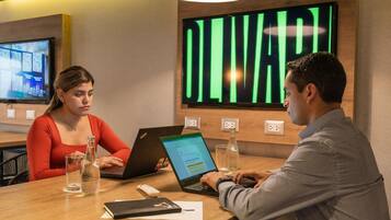 A conference room with a large digital display, a television, and a wooden table with laptops, glasses, and a bottle.