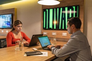 A conference room with a large digital display, a television, and a wooden table with laptops, glasses, and a bottle. - Casa Andina Standard Trujillo Plaza (Trujillo)