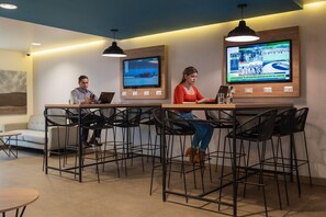 A modern lounge area with a long table, black chairs, and two large screens displaying sports content. - Casa Andina Standard Trujillo Plaza (Trujillo)
