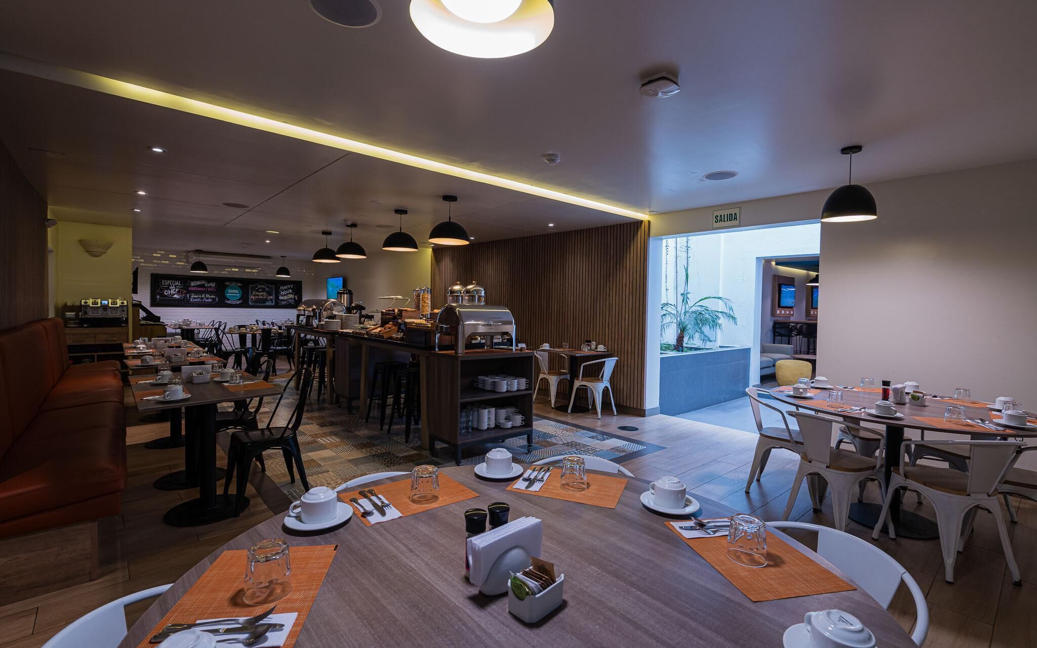 Un moderno comedor de hotel con varias mesas, una estación de café y vistas al exterior.