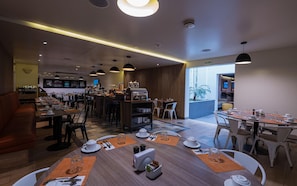 A modern hotel dining area with multiple tables, a coffee station, and a view of the outdoors. - Casa Andina Standard Trujillo Plaza (Trujillo)