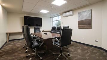 A conference room with a large table, six chairs, a flat-screen TV, and a window.