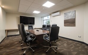 Un salón de conferencias con una mesa grande, seis sillas, un televisor de pantalla plana y un ventanal.