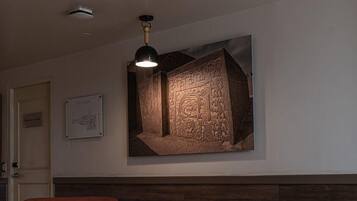 A room with a ceiling fan, a small table, two chairs, a wall-mounted artwork, and a door labeled 'Equipment Storage'.