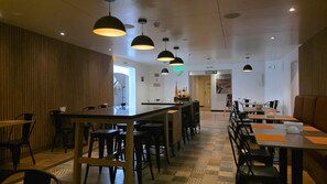 Interior de restaurante com área de bar, várias mesas e cadeiras.