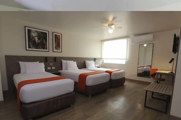 A hotel room with two beds, a ceiling fan, a large window, a mirror, and a small table.
