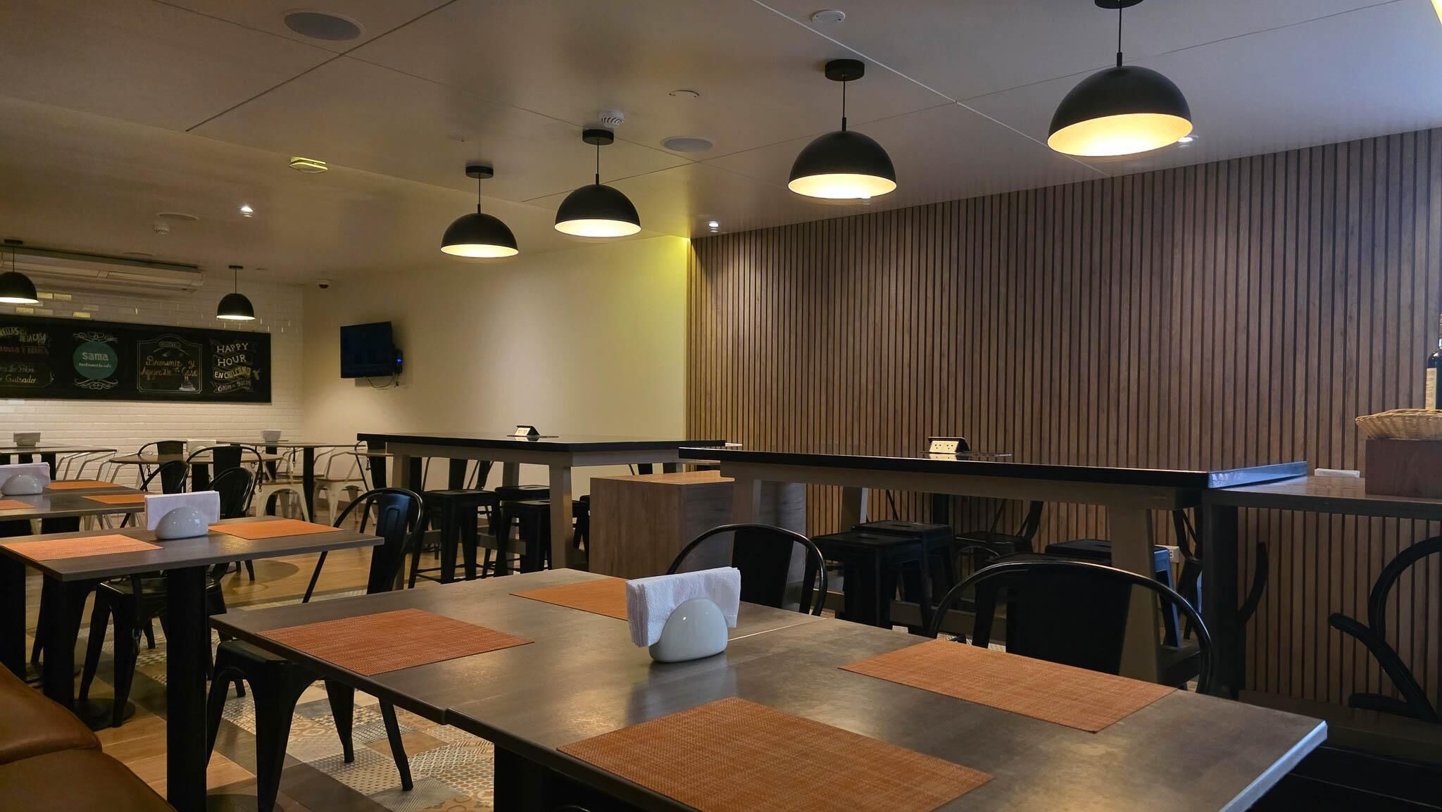 A restaurant interior with tables, chairs, pendant lighting, a counter, and a chalkboard menu.