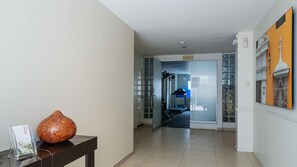 Um corredor de hotel com uma receção, um grande vaso decorativo e uma porta de vidro que dá para uma sala de ginástica.
