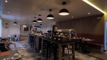 A modern cafe interior with a central bar, multiple seating options, and a television screen in the background.