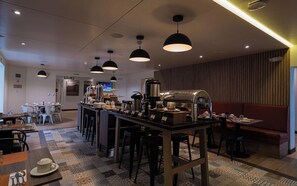 A modern cafe interior with a central bar, multiple seating options, and a television screen in the background. - Casa Andina Standard Trujillo Plaza (Trujillo)