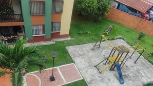 A playground with a slide and climbing structure, surrounded by a green lawn and a brick wall. - El Confort (Cali)
