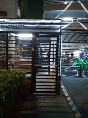 Une entrée abritée avec un portail en métal, un escalier menant à l’intérieur et un sapin de Noël décoré de guirlandes lumineuses.