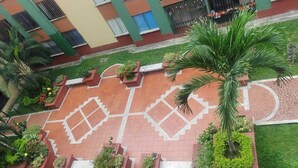 A courtyard with a geometric tile pattern, surrounded by planters with various plants and a palm tree. - El Confort (Cali)