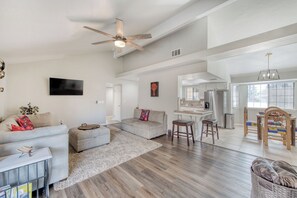 A spacious living room with a ceiling fan, a grey sofa, a coffee table, and a dining area with a wooden table and chairs. - Casa Barrera Soothing 3-Bedroom Home in a North East Fresno! (Fresno)