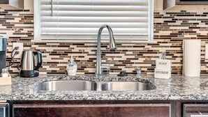 Cocina con encimera de granito, pileta de acero inoxidable y salpicadero de azulejos.