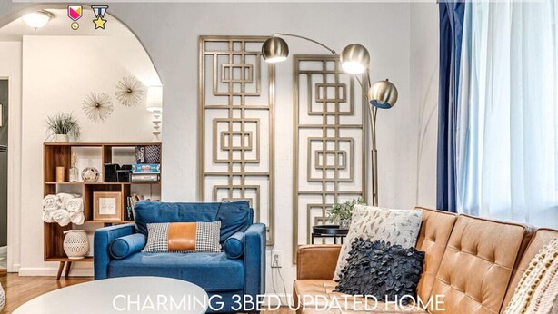 Una sala moderna con un sofá azul, un sofá de cuero marrón y una mesa de centro blanca. Se observa un panel decorativo en la pared y una lámpara de pie.