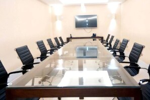 A conference room with a long glass table, black chairs, a flat-screen TV on the wall, and a projector.