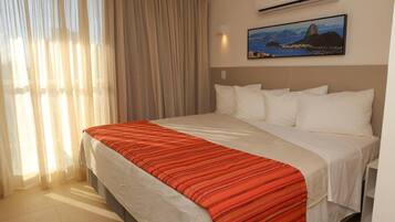 A hotel room with a bed, curtains, an air conditioning unit, and a wall-mounted picture.