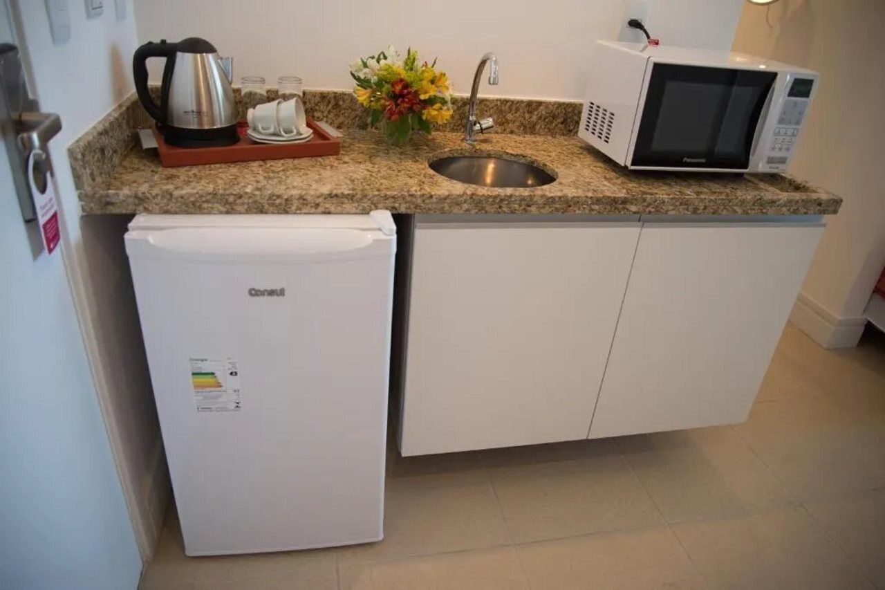A compact kitchen with a built-in refrigerator, a microwave, a kettle, and a sink.