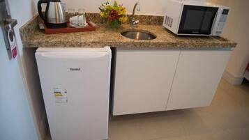 A compact kitchen with a built-in refrigerator, a microwave, a kettle, and a sink.