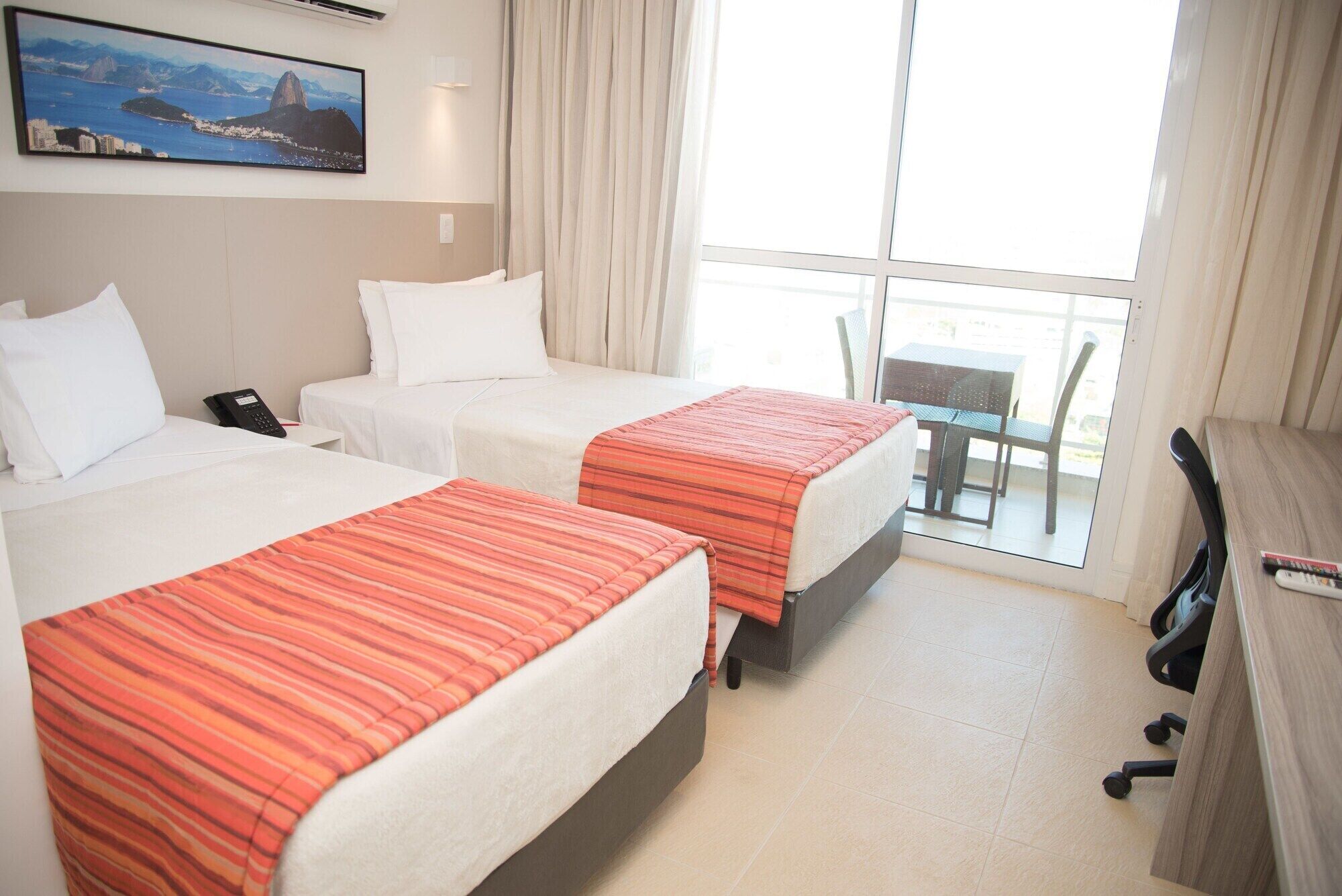 Een hotelkamer met twee bedden, een bureau, een stoel en uitzicht op de stad.