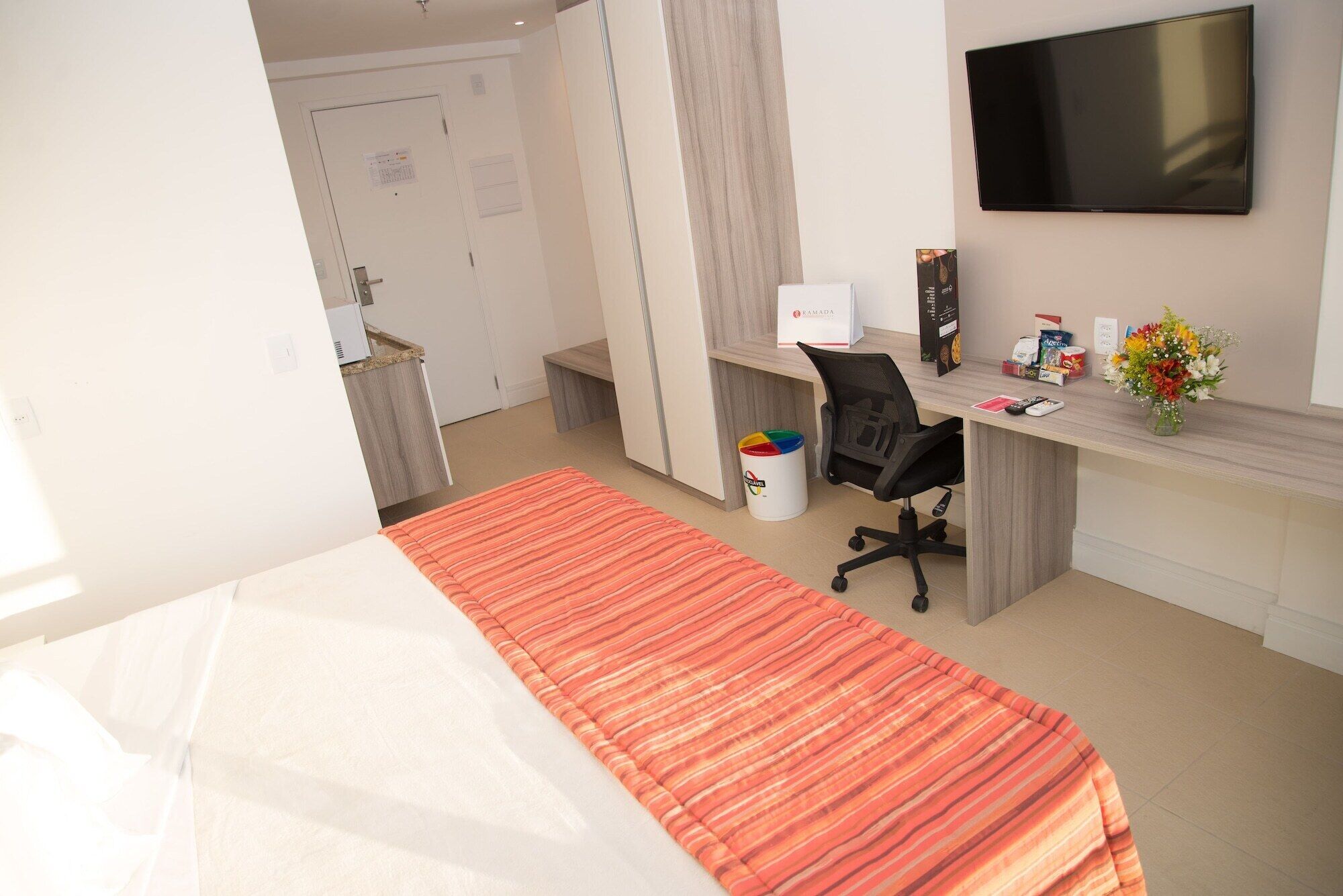 Ett hotellrum med en säng, ett skrivbord, en stol, en tv och en papperskorg.