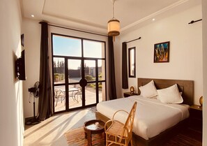 A bedroom with a large bed, a wooden floor, a fan, a table with a candle, and a view of the outdoors through a glass door. - Guesthouse Dar Ayman Essaouira B&B (Essaouira)