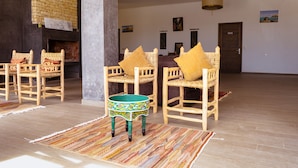A spacious living area with a fireplace, wicker furniture, and a colorful woven table. - Guesthouse Dar Ayman Essaouira B&B (Essaouira)