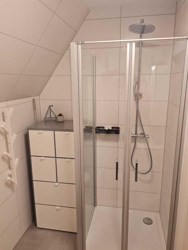 A modern shower enclosure with a glass door, a small cabinet with drawers, and a showerhead.