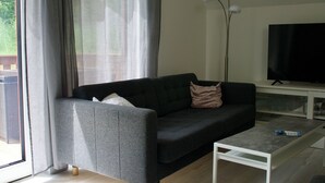 A living room with a dark grey sofa, a white coffee table, and a flat-screen TV on a stand.