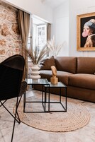 A modern living room with a brown sofa, a glass coffee table, a black chair, a woven rug, and a vase with dried plants.