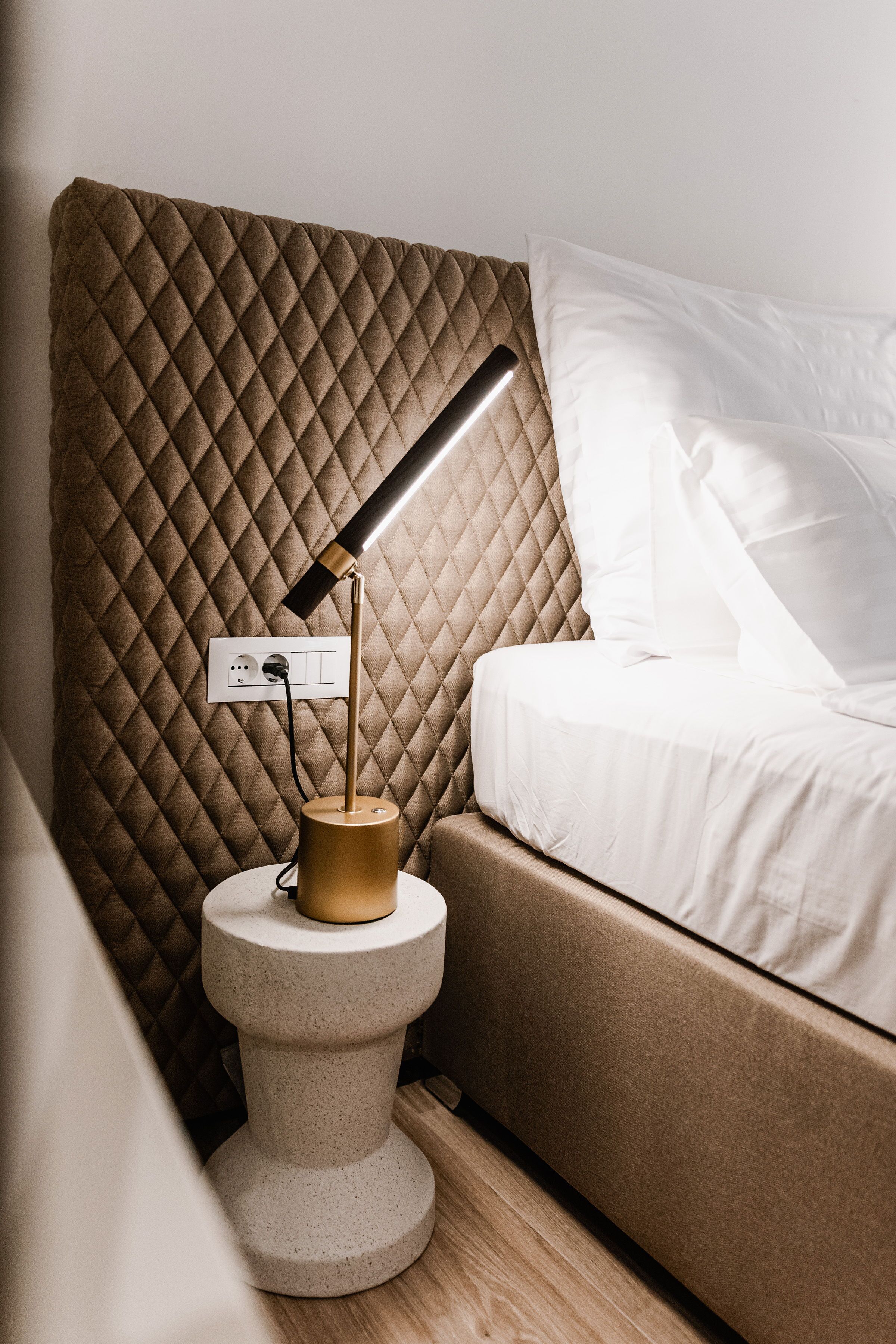 Een moderne slaapkamer met een gewatteerd hoofdeinde, een bedlampje en een wit bed.