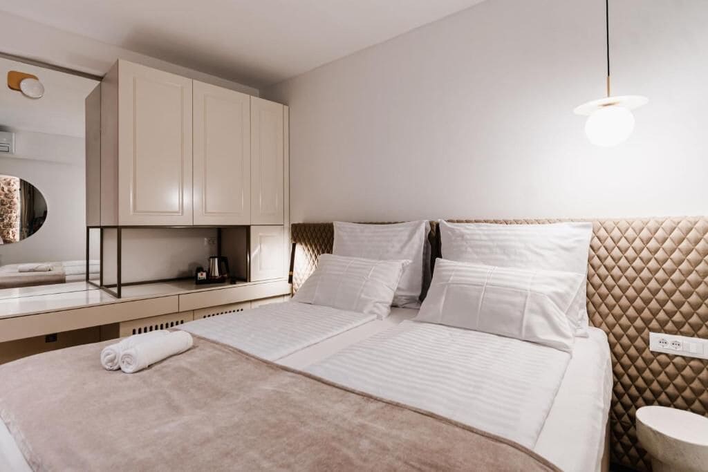 A modern hotel room with a large bed, a desk with a coffee machine, and a wall-mounted cabinet.