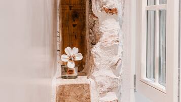 A stone wall with a wooden beam, a white door with a brass handle, and a small table with a white flower and a candle.